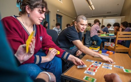 An image of 2 students playing a card game on a coffee table.